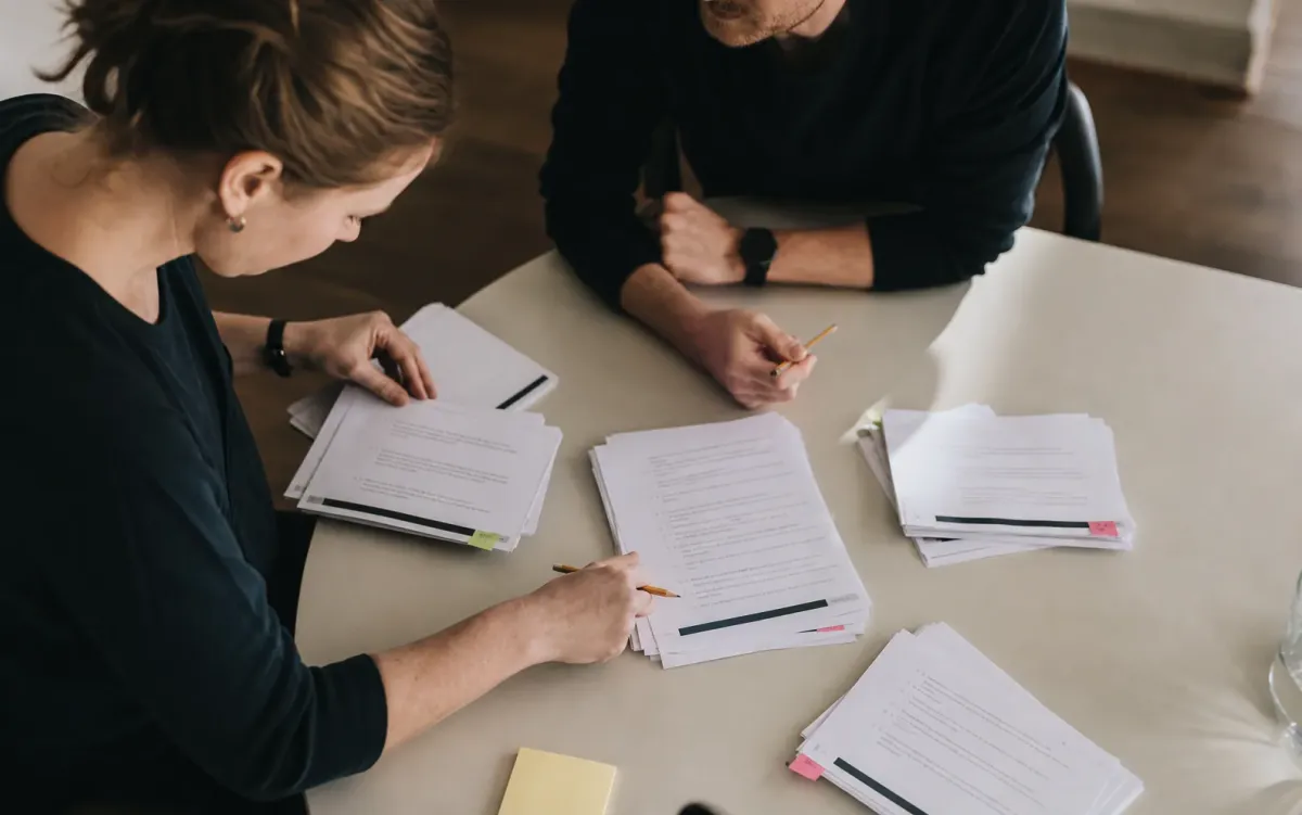 Zwei Personen prüfen und ordnen schriftliche Fragen am Tisch.