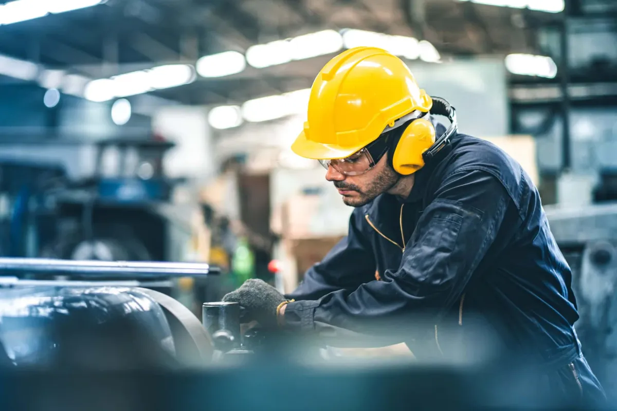 Industriearbeiter mit gelbem Schutzhelm an einer Maschine in einer Produktionshalle
