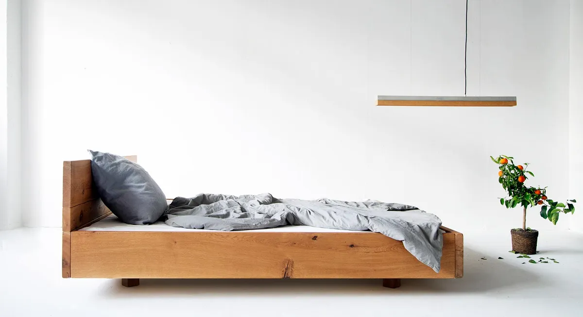 Holzbett mit grauer Bettwäsche und Pendelleuchte in einem hellen Raum