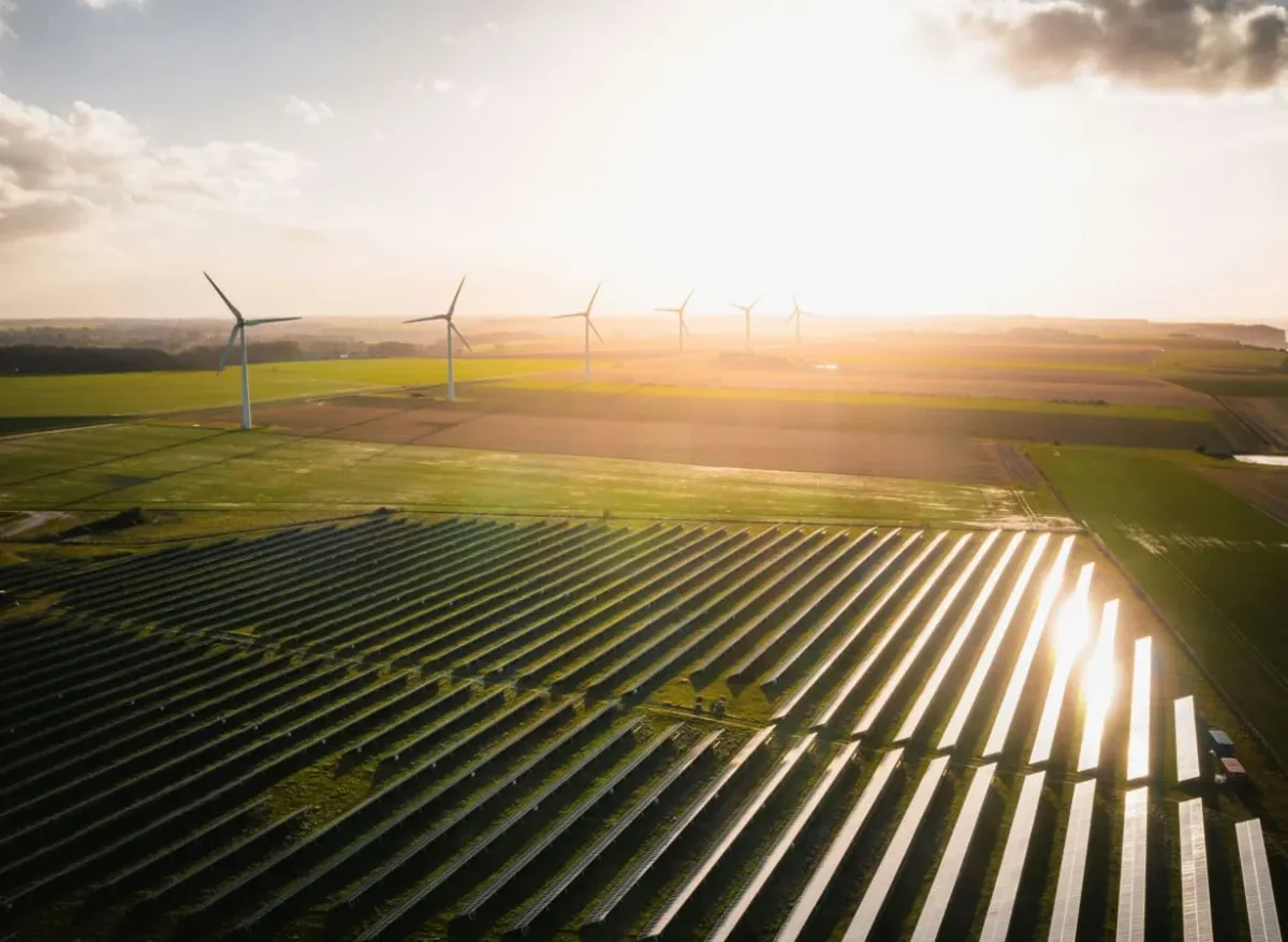 Luftaufnahme eines Solarparks mit Windkraftanlagen im Abendlicht